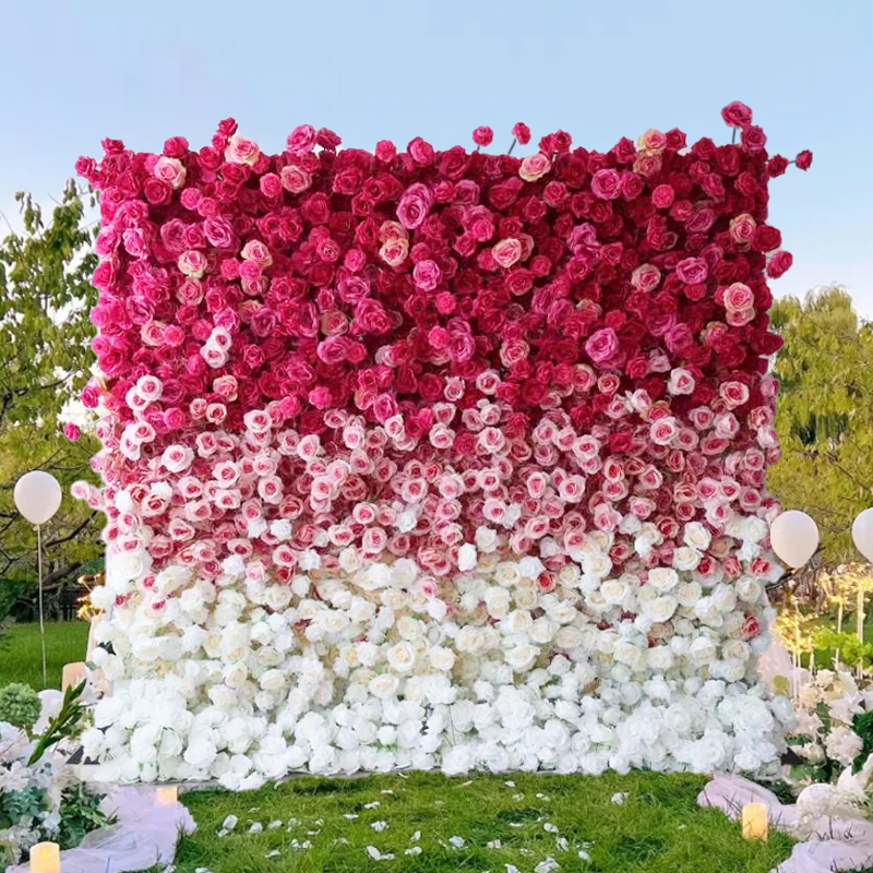 An outdoor wedding with a pink and white gradient flower wall creates a beautiful background